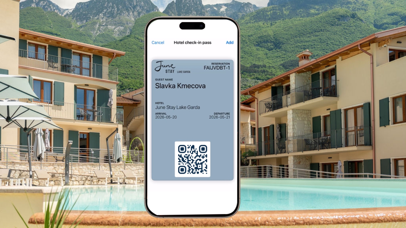 A phone showing a hotel check-in wallet pass in front of a sunlit lakeside hotel