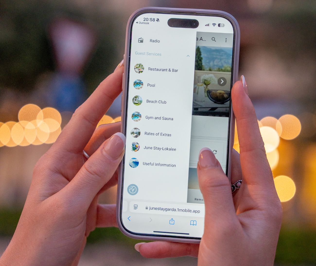 A hotel guest arriving in the evening, holding a phone that shows the property's digital guest-services menu