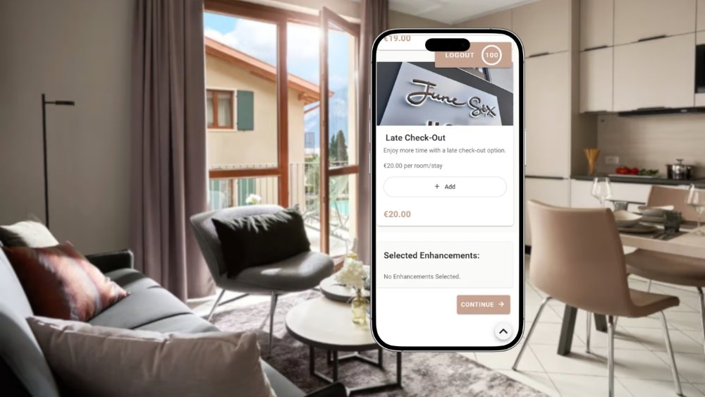A smartphone showing a Late Check-Out add-on for €20 per room on departure day, over a sunlit June Six apartment interior