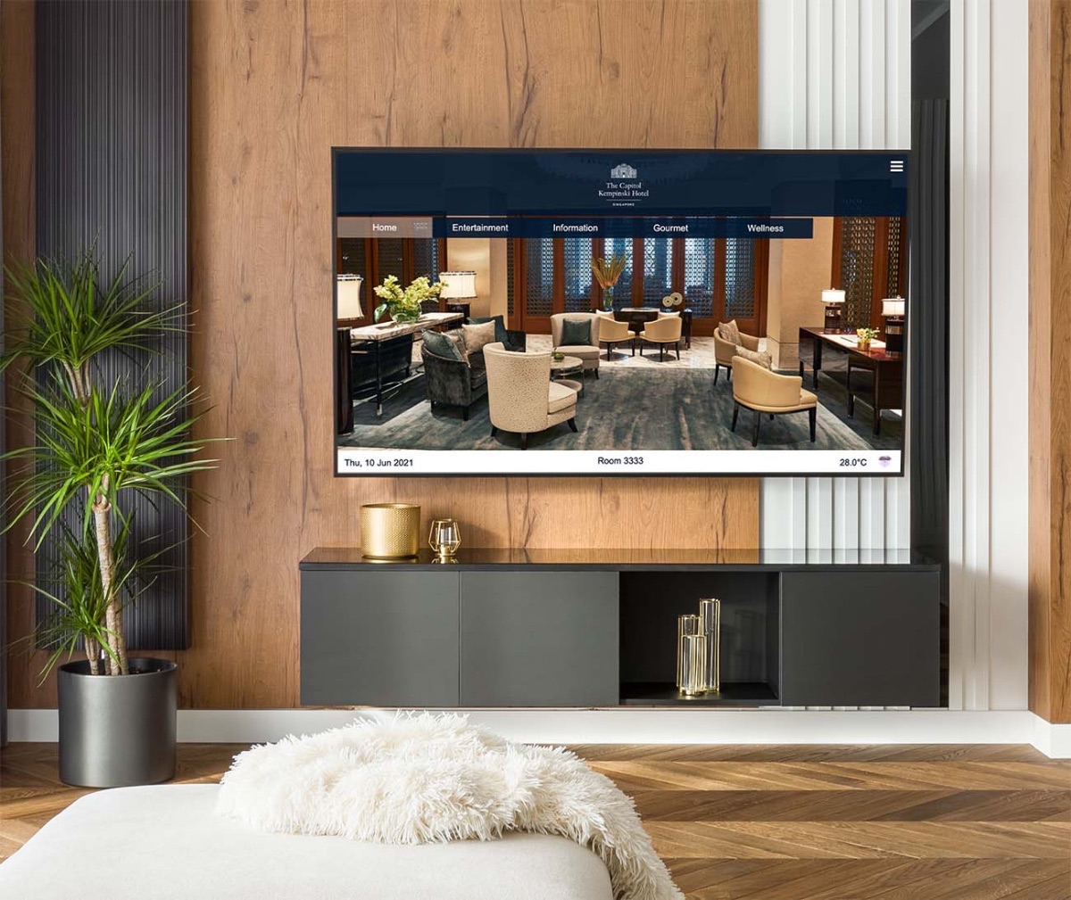 An in-room hotel TV showing The Capitol Kempinski Singapore branded interface, mounted on a wood-panelled wall