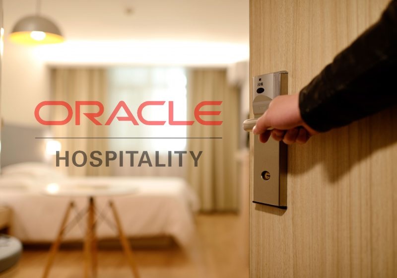 A hand on a hotel room door handle with the Oracle Hospitality wordmark