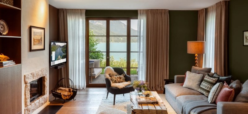 A Rosewood Schloss Fuschl suite with an in-room TV, a fireplace and a window onto Lake Fuschl